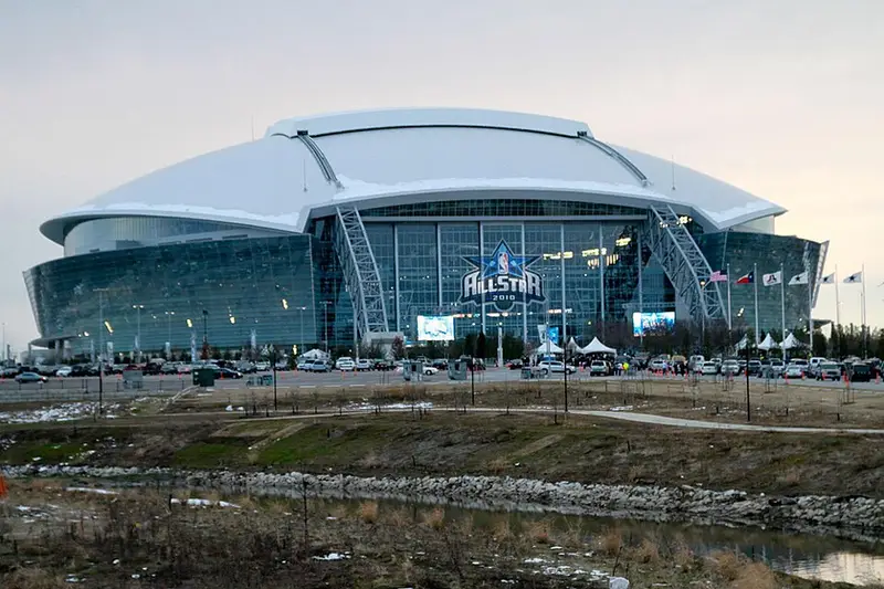 阿靈頓 AT&T Stadium（2026 世界盃 Dallas Stadium）封面視覺：夕陽球場外觀與城市背景，前景含公路指標、交通車輛與地圖定位元素，並以圖示呈現賽程、交通、周邊與完整攻略重點